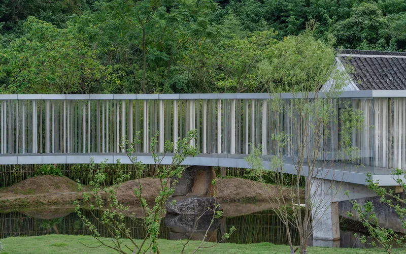 Elevated walkway with vertical metal batten screen reflected in still water below