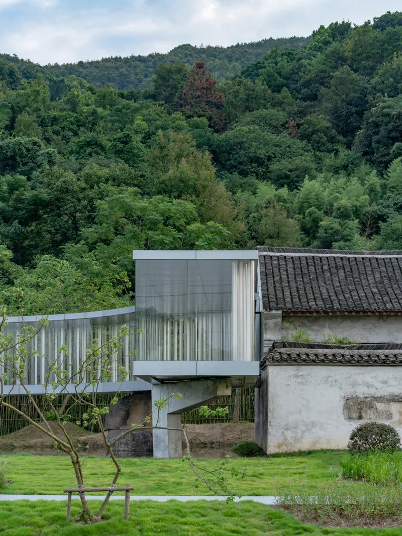 Concrete and glass volume cantilevered over stone foundation against forested hillside