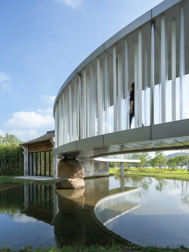 Curved glass balustrade with vertical mullions spanning a reflecting pool with figure visible inside