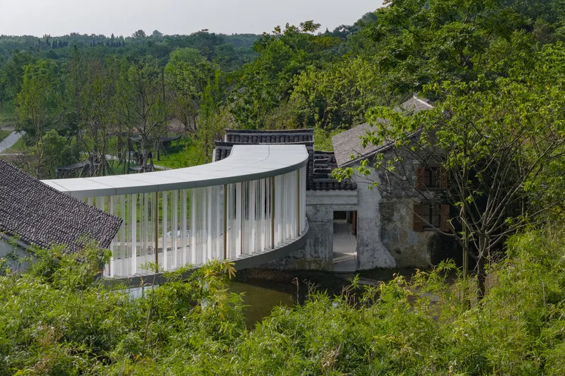 Elevated view of the curved pavilion bridging between restored masonry structures amid dense tree canopy