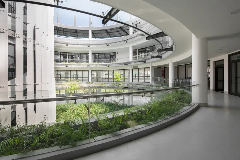 Interior atrium with sunken planted beds and circular skylight framed by white columns and glass railings