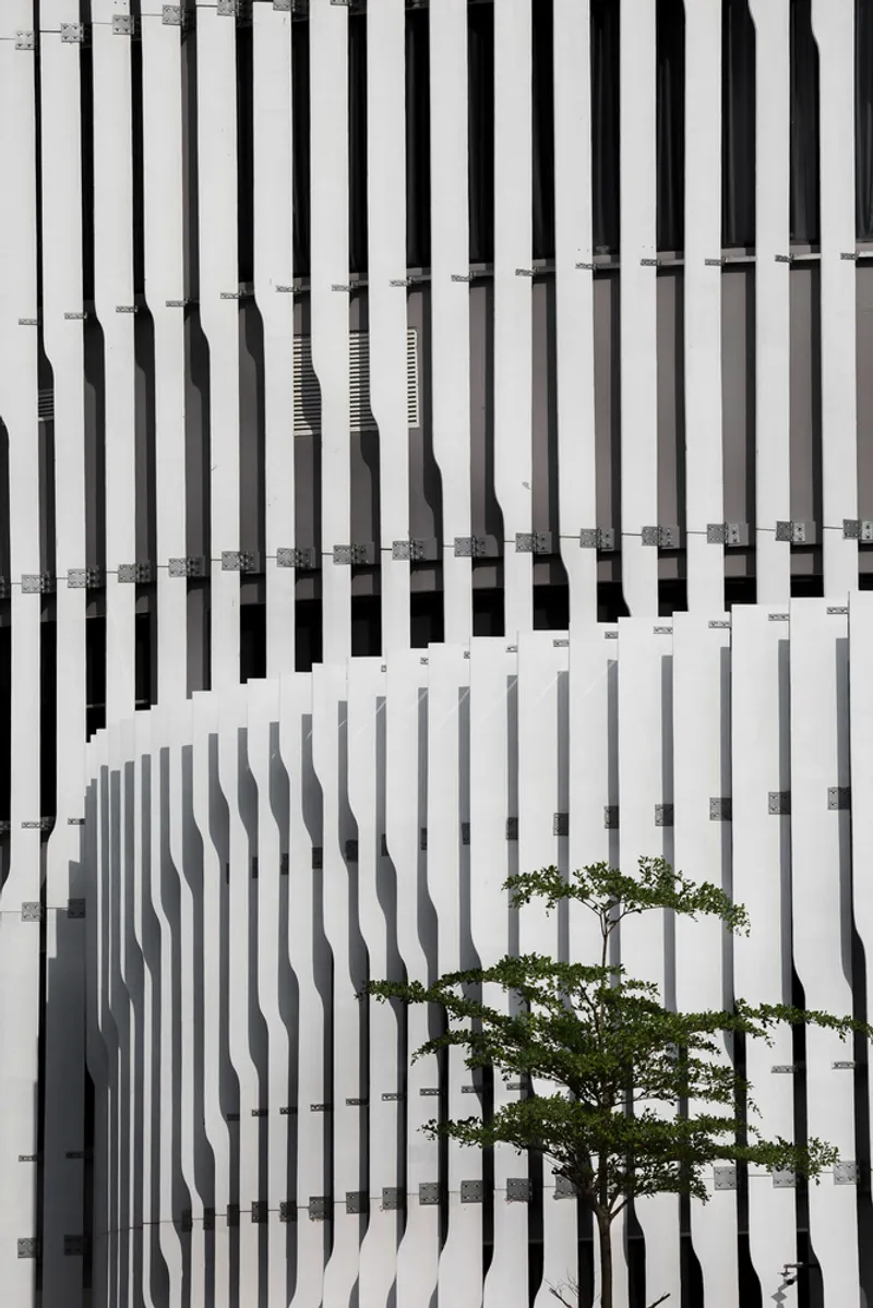 Vertical white brise-soleil facade with sculptural fins framing a tree against the screen