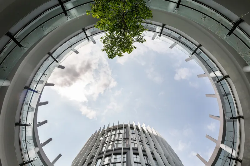 Upward view through circular courtyard opening showing ringed balconies and sky with clouds and tree canopy