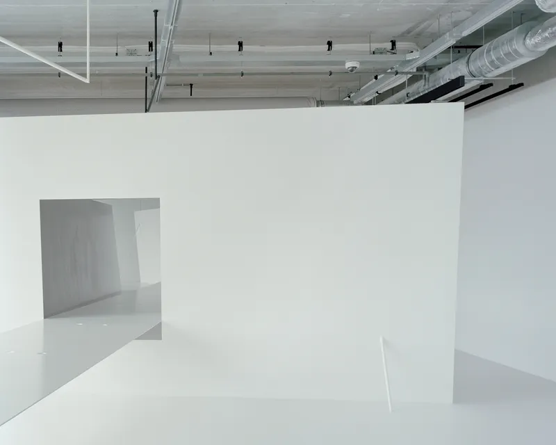 White partition walls creating angular openings beneath exposed mechanical ducts and ceiling panels