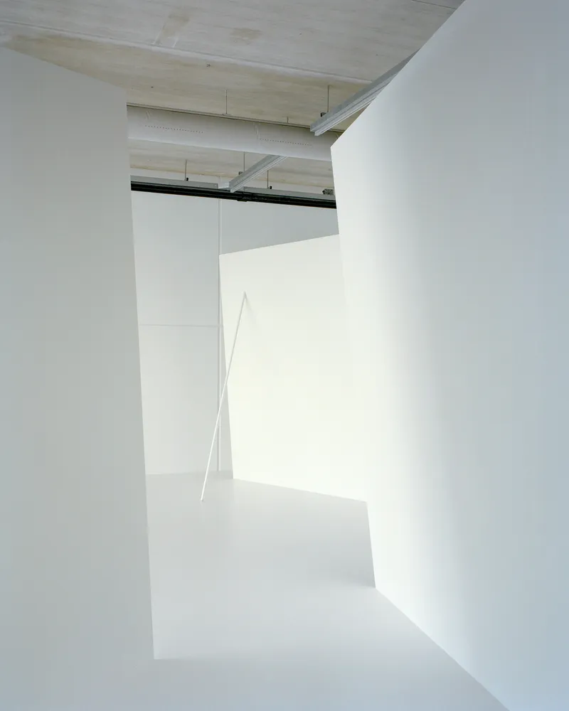 Narrow passage between angled white walls with a thin diagonal beam of sunlight