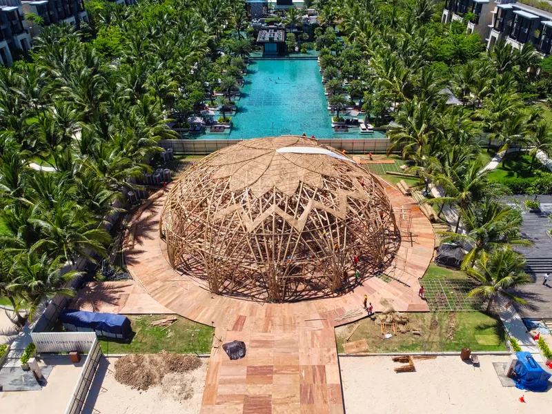 Aerial view of the woven bamboo dome pavilion surrounded by palm trees and a pool