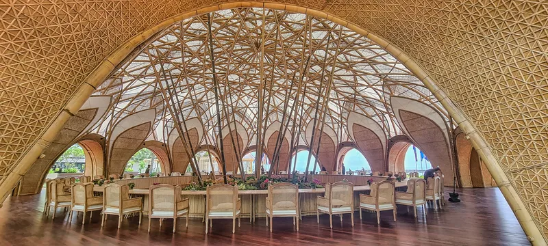 Interior dining hall with radial bamboo lattice dome overhead and arched openings along the perimeter