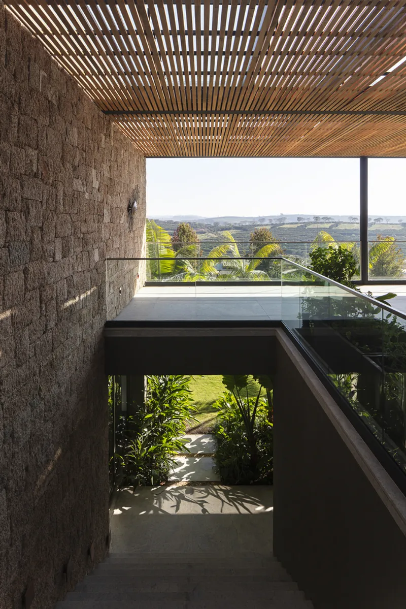 Stairwell with timber slatted ceiling and textured stone wall descending to a planted courtyard below