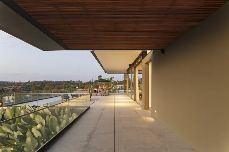 Covered outdoor walkway with timber ceiling and planted terrace bed at dusk