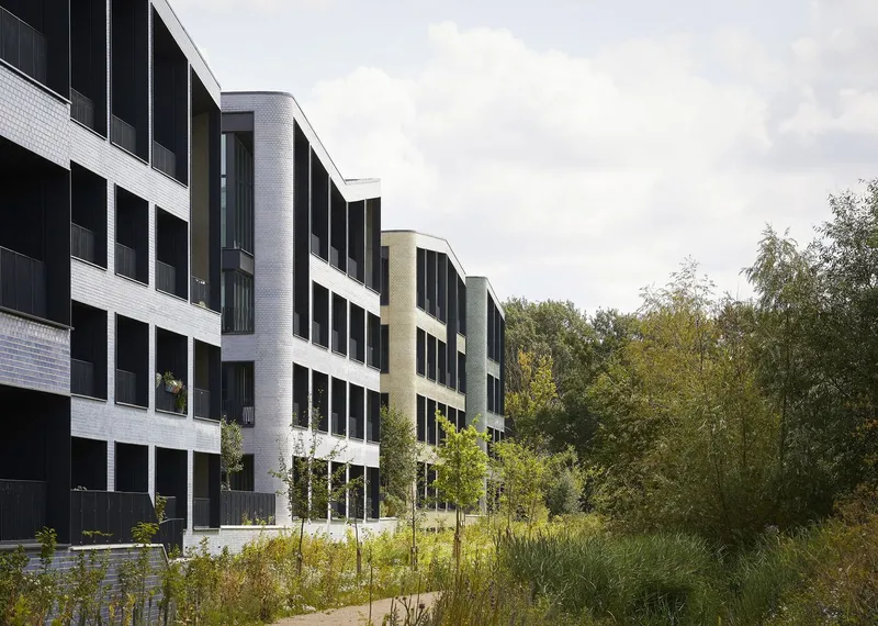 Facade with alternating grey and white brick volumes framed by a planted bioswale with grasses and trees