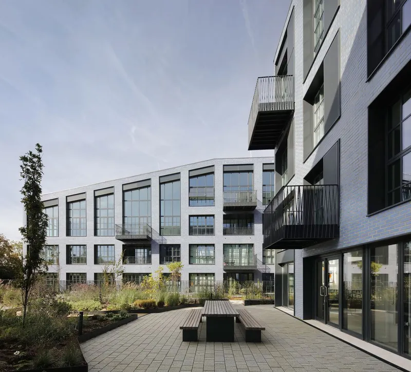 Courtyard with timber bench and paving facing arched facade volumes and cantilevered black balconies