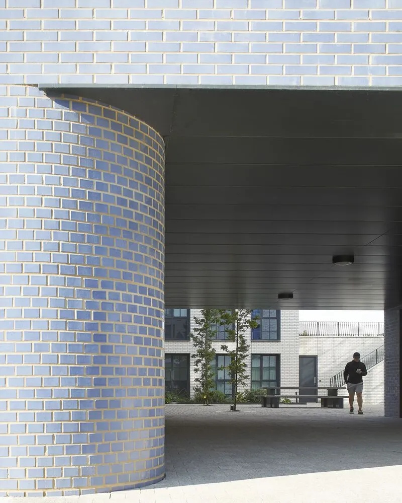 View through covered passageway framed by a curved pale brick column and dark soffit with a figure beyond