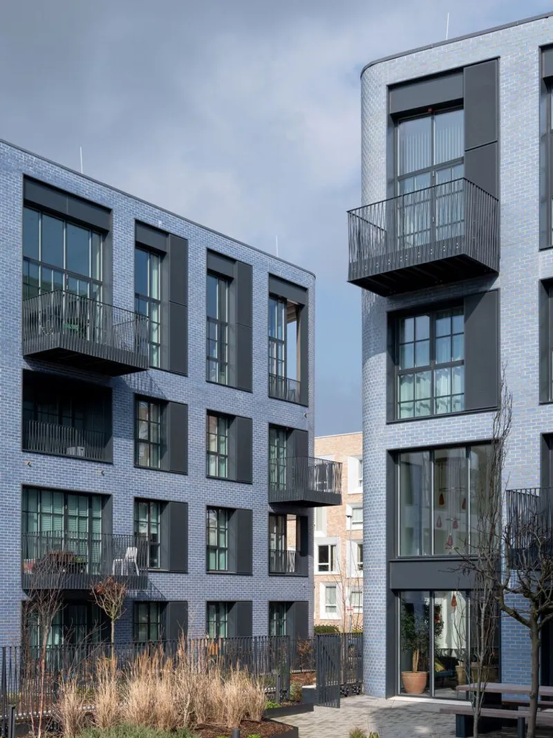 Facade detail showing metal balconies projecting from pale brick volumes with mullioned windows at dusk