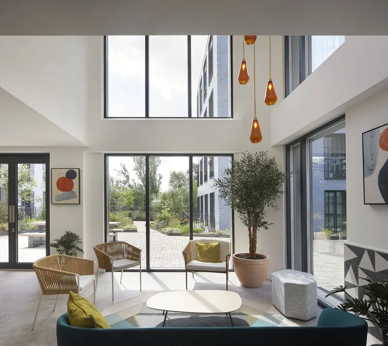 Double-height lobby with clerestory windows, amber pendant lights and potted tree overlooking the planted courtyard