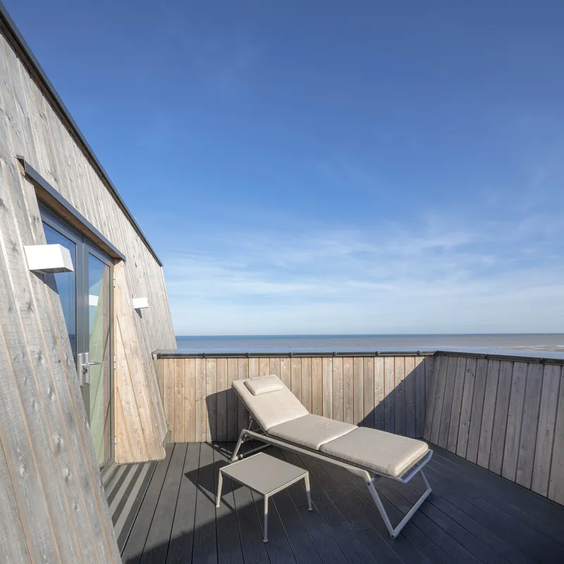 Rooftop deck with timber cladding and lounge chair facing the ocean under clear blue sky