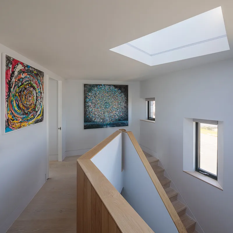 Upper landing with timber staircase balustrade and rectangular skylight above white walls