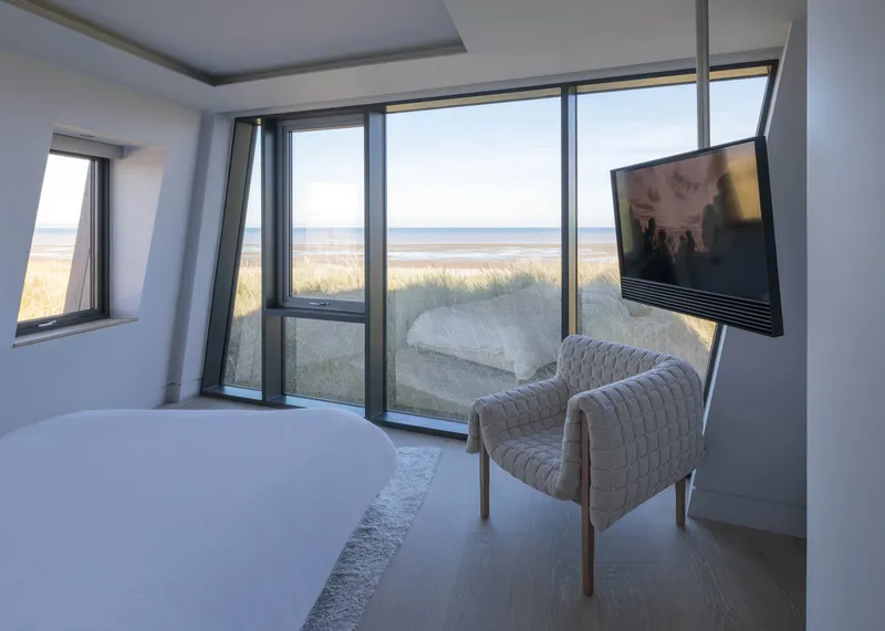 Bedroom with floor-to-ceiling glazing overlooking sand dunes and beach grasses