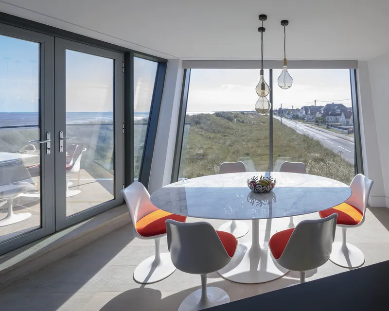 Dining area with canted windows and pendant lights facing dunes and neighboring houses