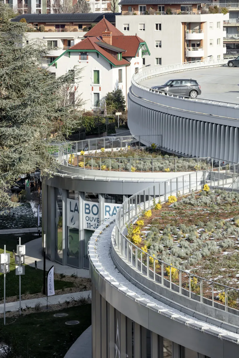 Spiraling green roof terraces with planted beds wrapping around the curved glazed facade