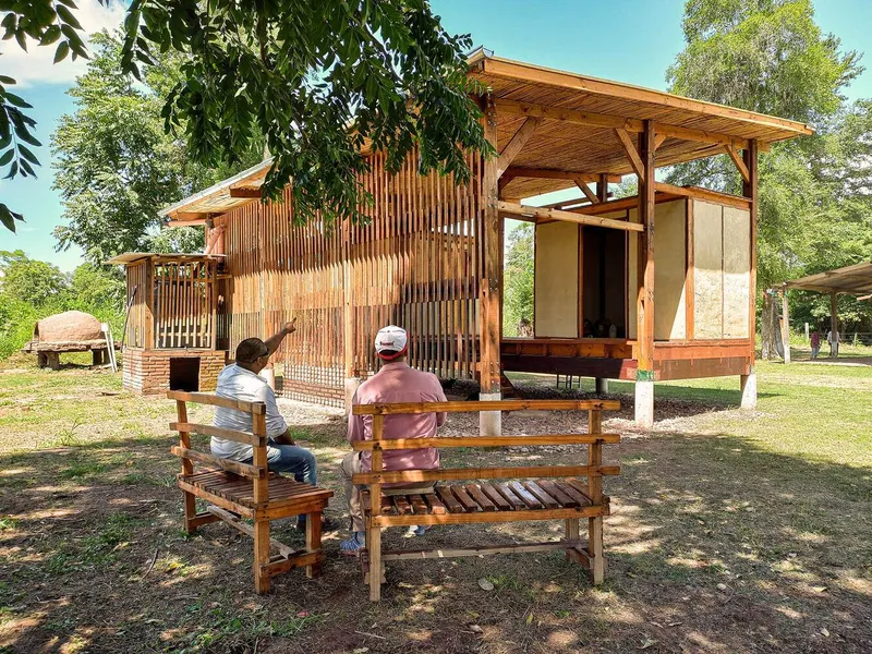 Timber-framed pavilions with vertical wood slat screens overlooking a grassy clearing with two seated figures