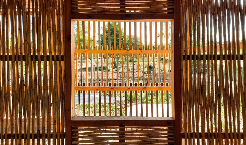 Layered timber slat screens framing a central window opening with filtered sunlight from the garden beyond