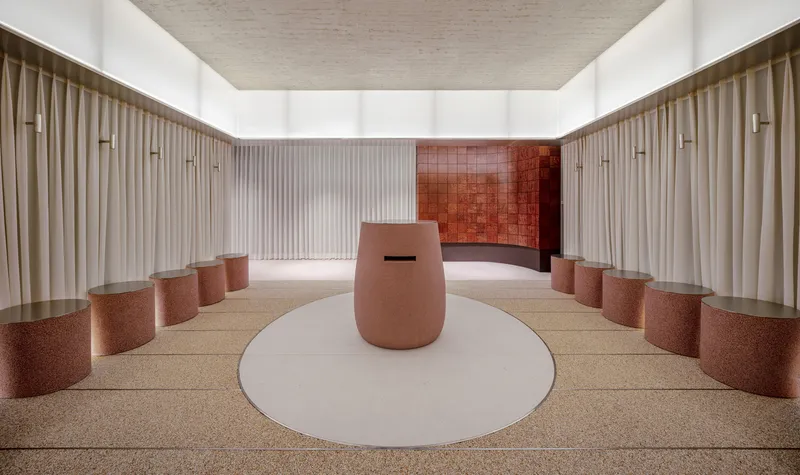 Dining hall with pink cylindrical stools flanking a white circular rug beneath a recessed ceiling