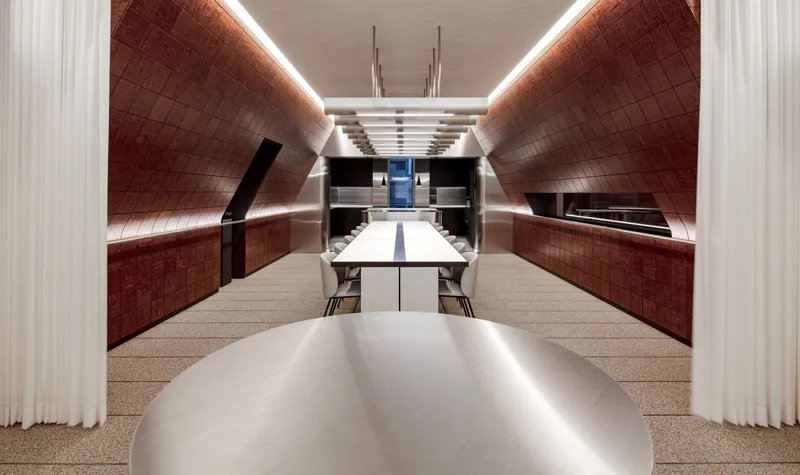 Long dining table with white surface running beneath curved red-tiled walls and suspended ceiling lights
