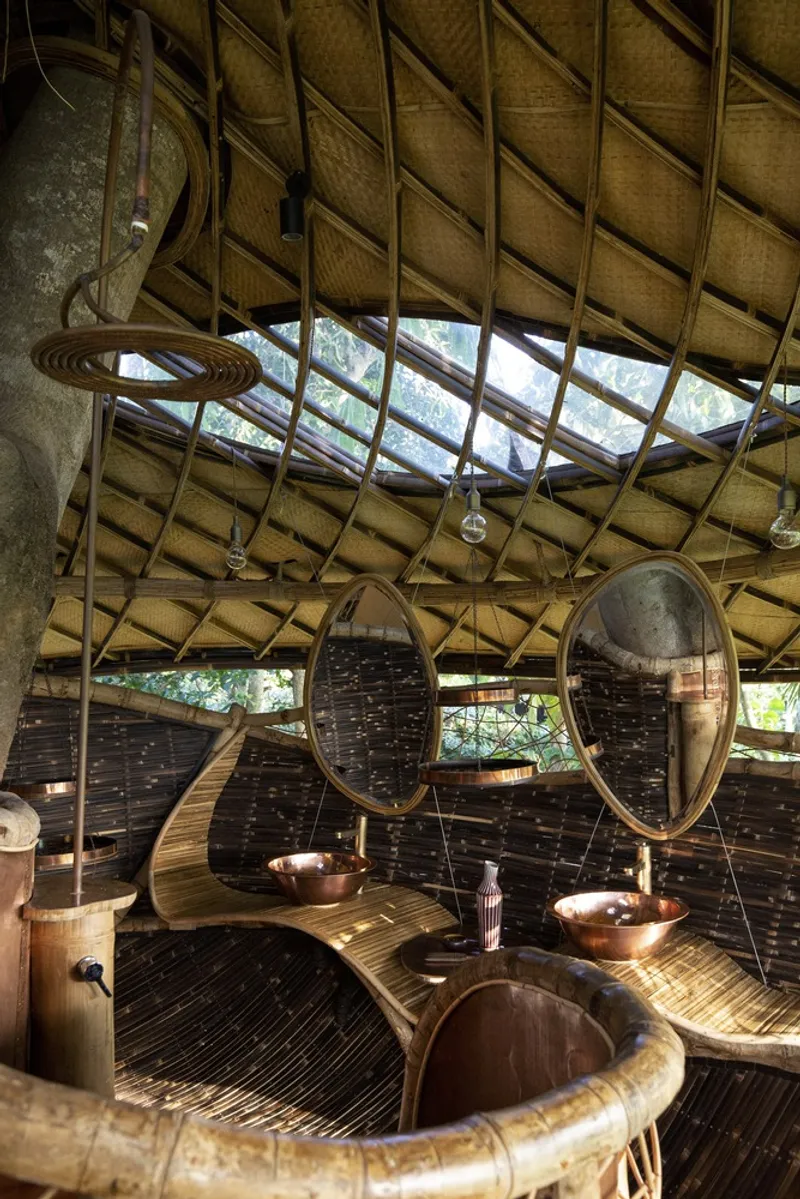 Bathroom interior with woven bamboo ceiling, skylight opening, copper bowl sinks, and oval bamboo-framed mirrors