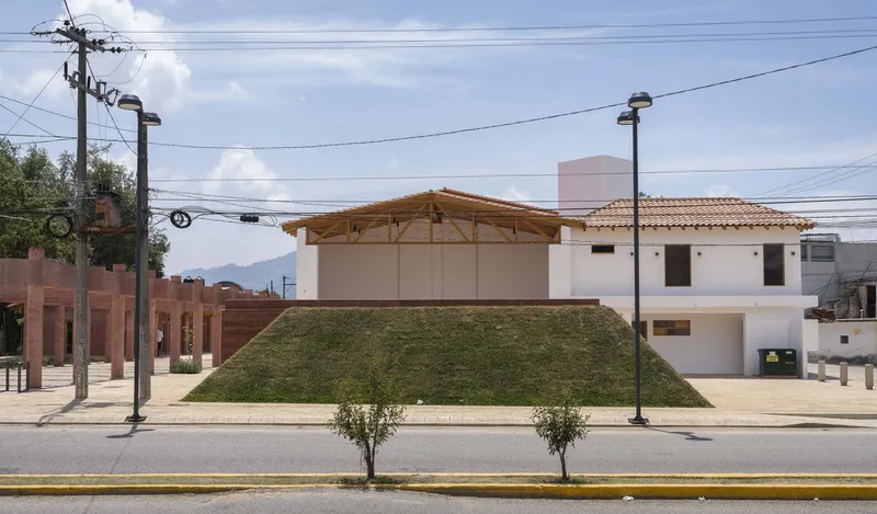 Street view of white stucco volumes with clay tile roofs set behind a sloped grass embankment