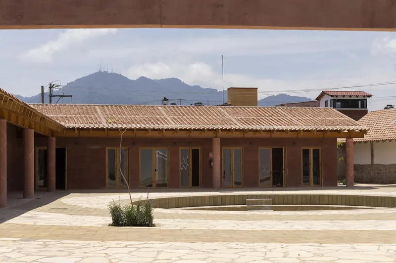 Courtyard facade with rammed earth walls and glazed doors beneath timber trusses and clay tile roof
