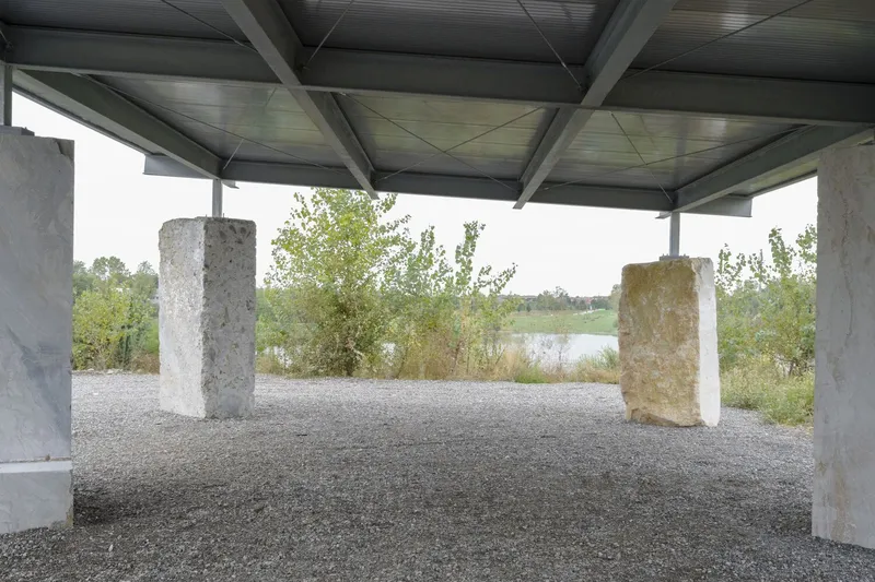 View through the pavilion toward a small pond framed by concrete columns and overhanging steel beams