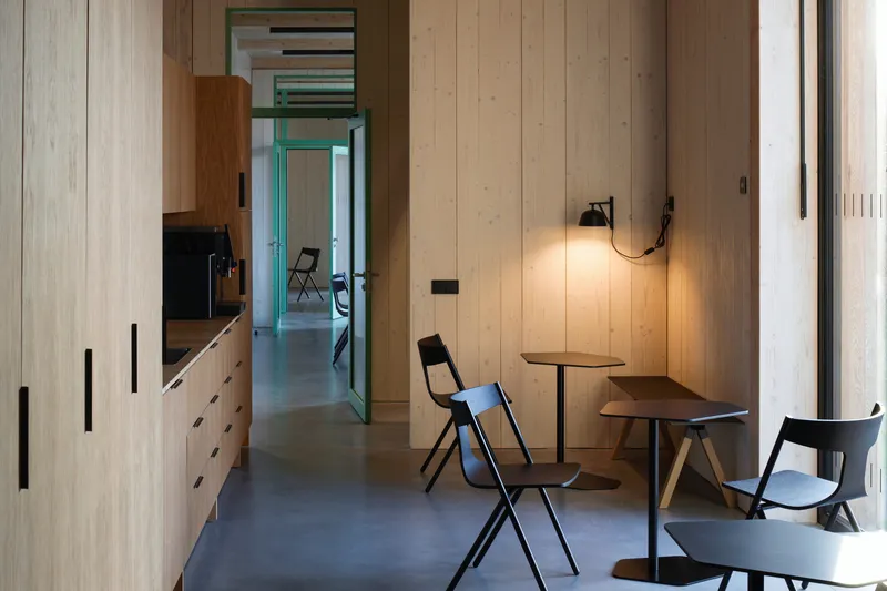 Interior corridor with timber cabinetry and a wall-mounted lamp beside small tables and folding chairs