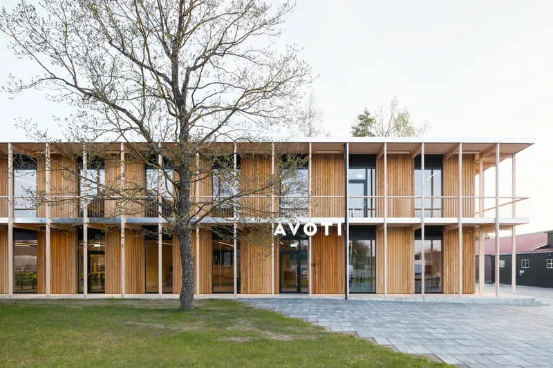 Two-storey timber-clad facade with vertical slat screens and white columns behind a bare tree in the plaza