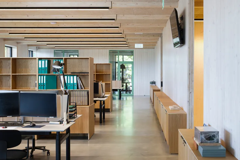 Open-plan office with timber shelving units and polished concrete floor under a slatted timber ceiling