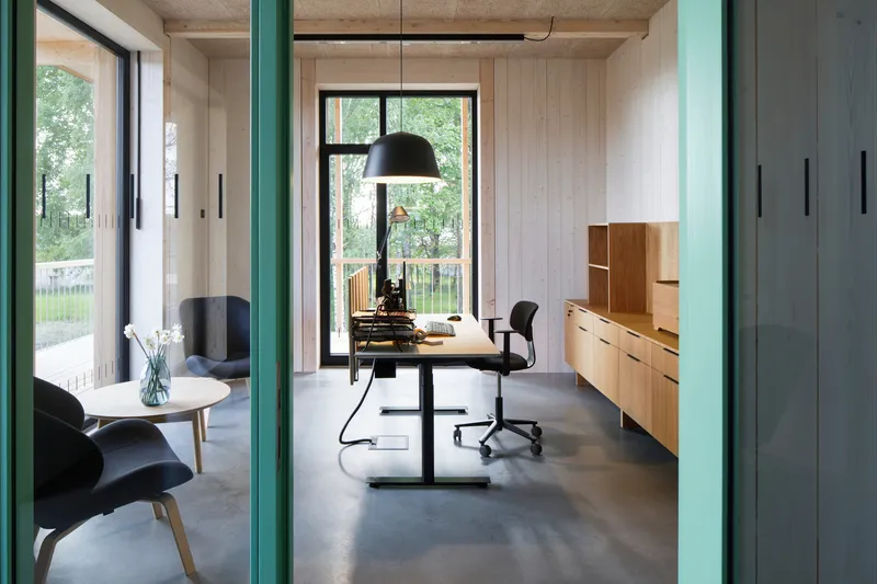 Office interior with exposed concrete ceiling, teal steel columns, and polished concrete floor opening to a garden