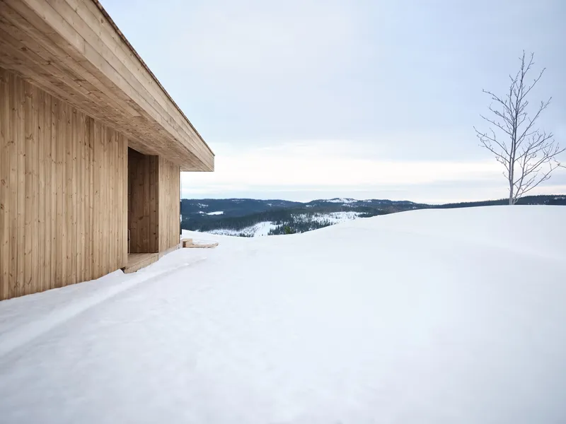 Timber-clad exterior wall with recessed entry opening overlooking a snow-covered landscape and distant hills