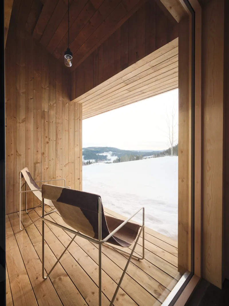 Canvas sling chair on timber deck framed by large window opening onto snowy terrain