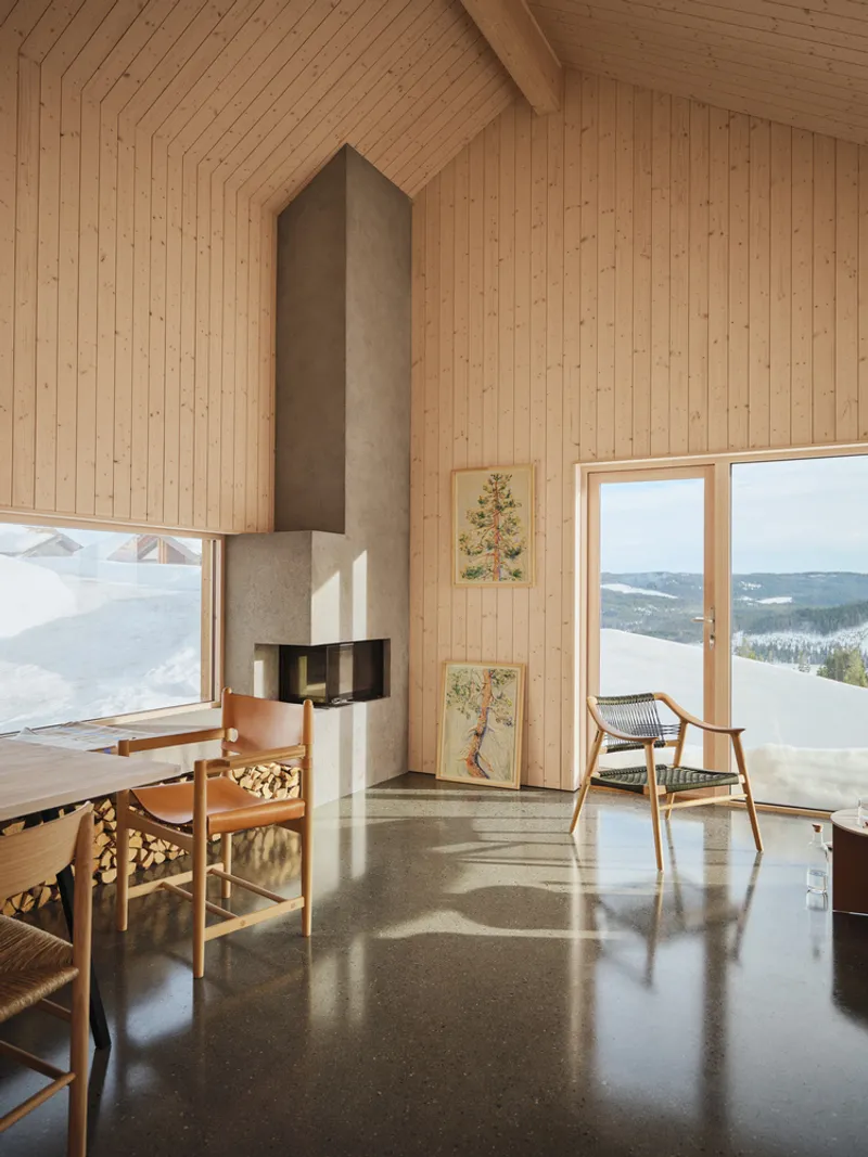 Living area with grey fireplace chimney, timber walls, and floor-to-ceiling windows framing winter views