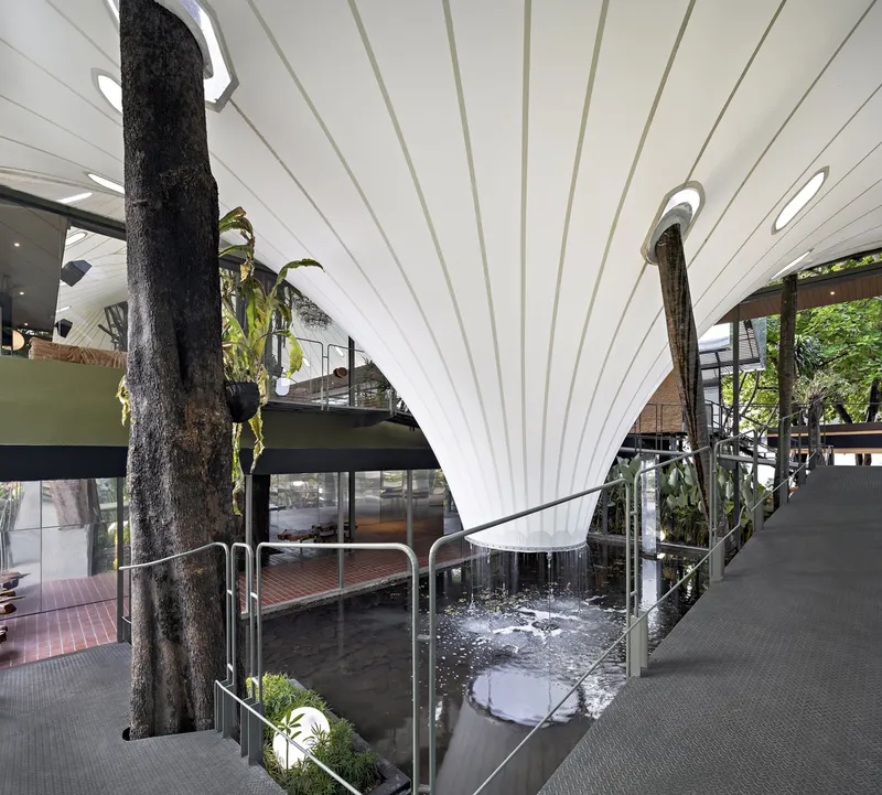 Interior view showing preserved tree trunks piercing through the ribbed white ceiling beside a water feature