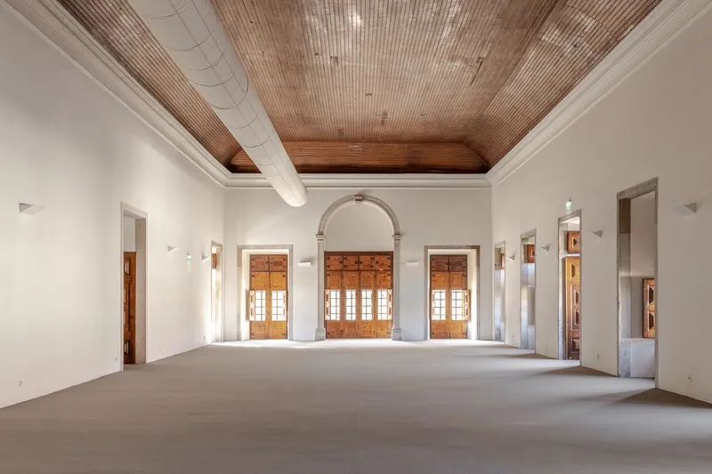 Interior hall showing timber ceiling with exposed beam and triple arched doorway flanked by wall sconces