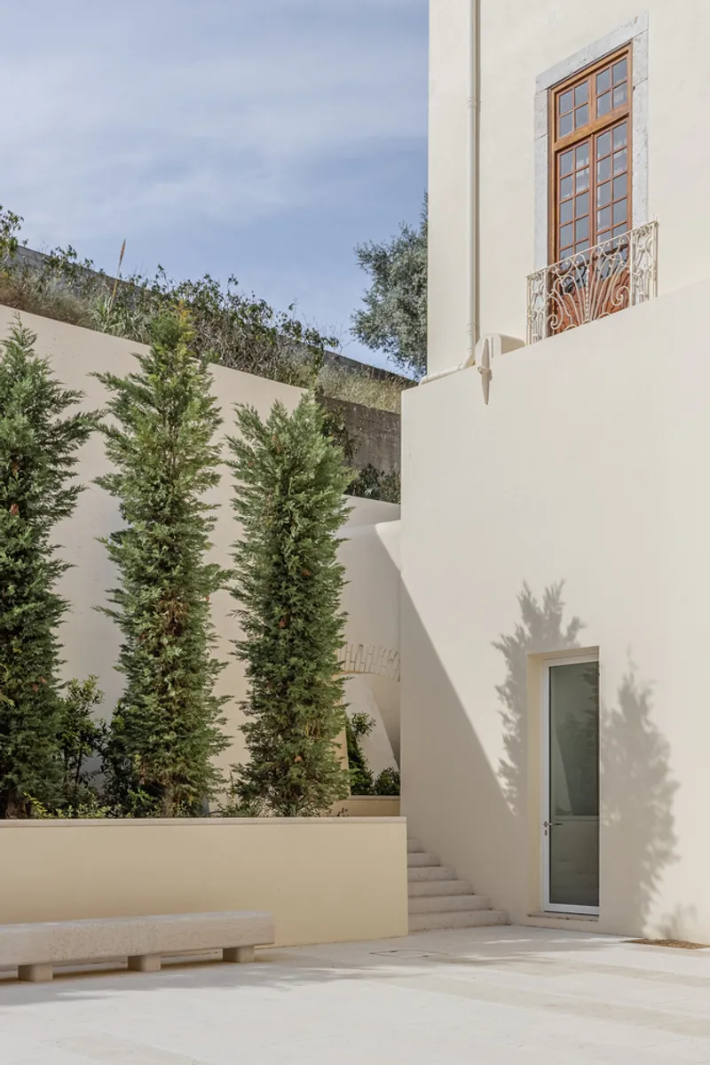 Courtyard with white stucco walls, a timber-framed window, cypress trees, and stone bench