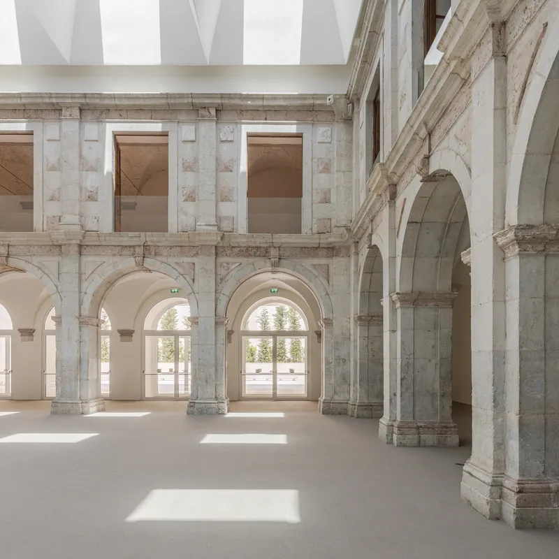 Two-story arcade with stone columns and arched openings casting shadows on the polished concrete floor