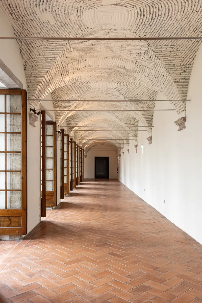 Long corridor with herringbone terracotta floor, exposed brick vaulted ceiling, and glazed timber doors