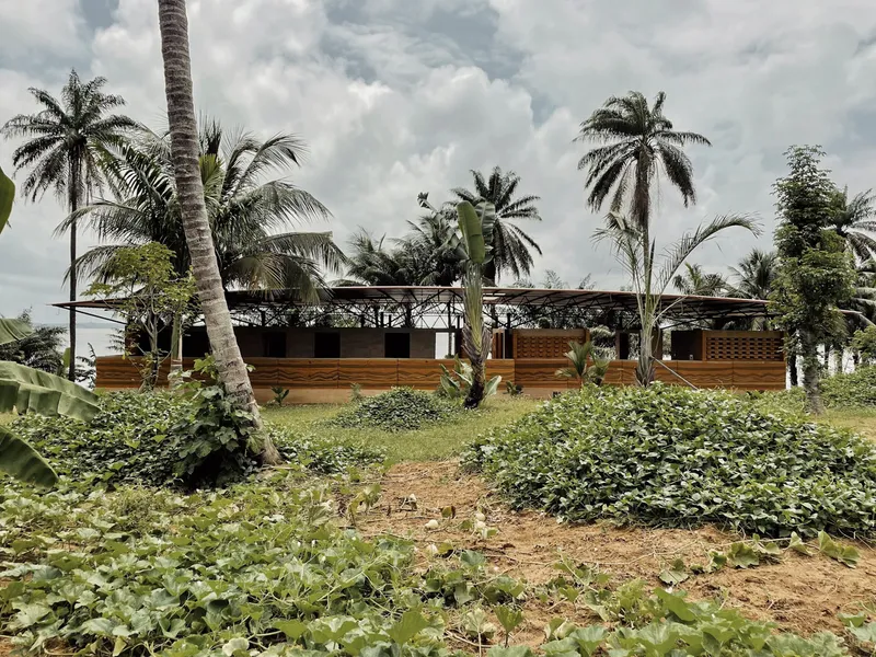 Timber and lattice facade with raised steel roof structure viewed across a vegetable garden