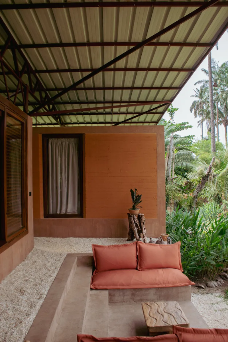 Covered porch with concrete bench seating and exposed steel truss canopy above rammed earth wall