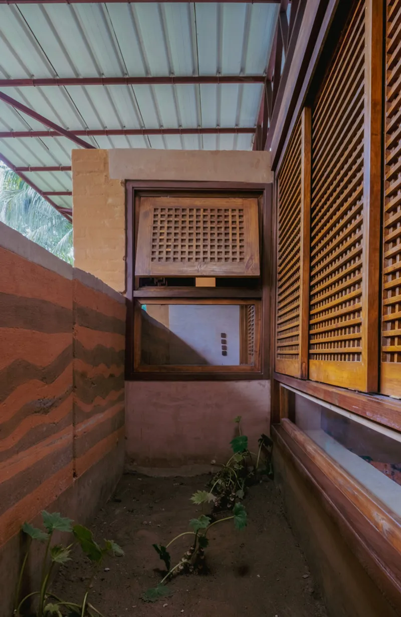 Narrow exterior passage with latticed timber screens and rammed earth wall holding potted plants