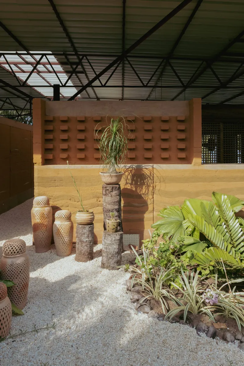 Courtyard with perforated rammed earth wall behind sculptural planters and tropical foliage in daylight