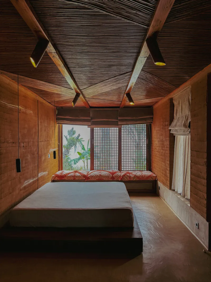 Bedroom with faceted timber ceiling, rammed earth walls, and window seat overlooking greenery