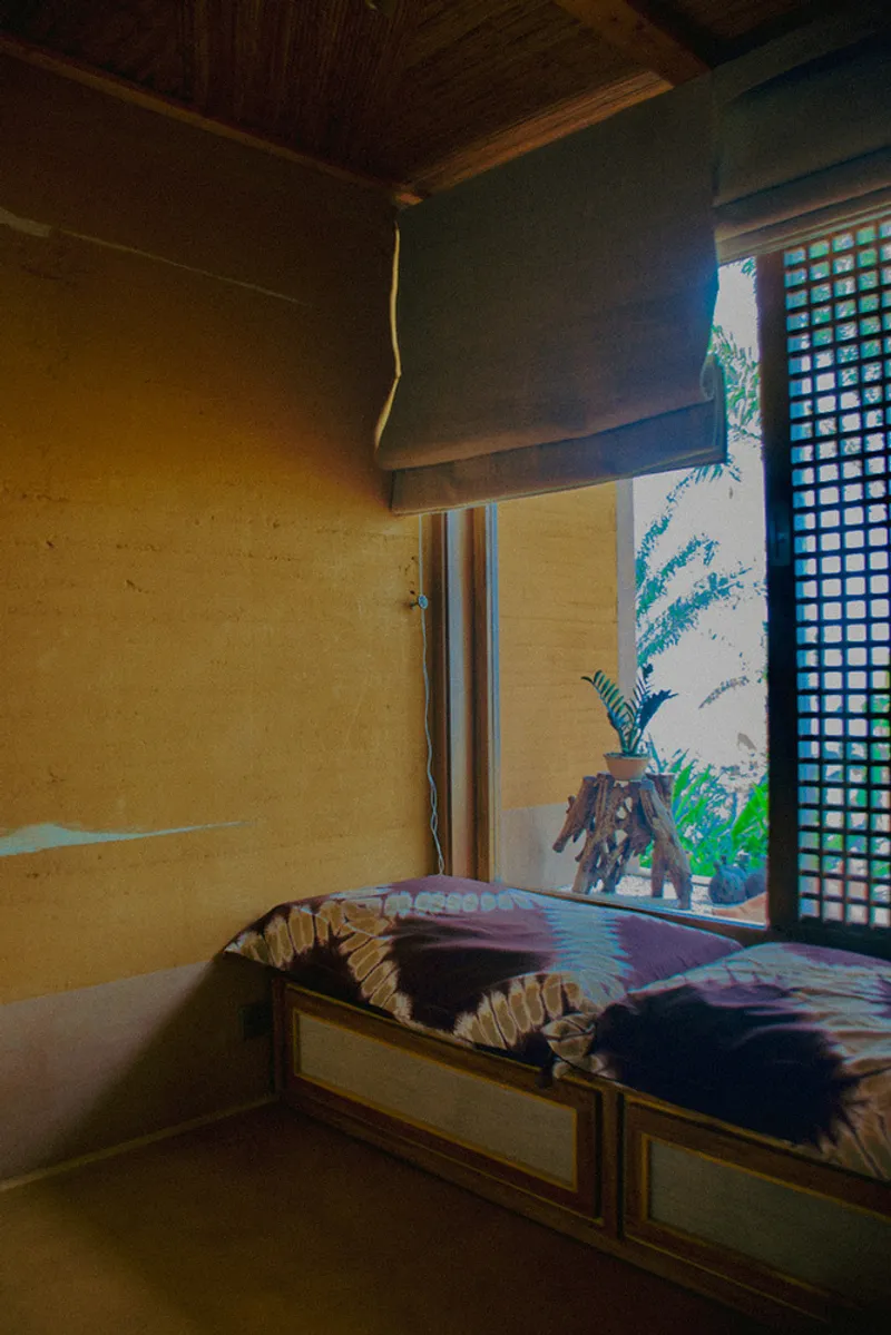 Built-in bed platform beside a latticed screen and mural of tropical foliage at dusk