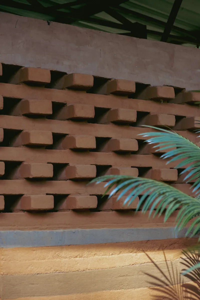 Perforated terracotta brick screen wall with palm fronds casting shadows below painted timber beams